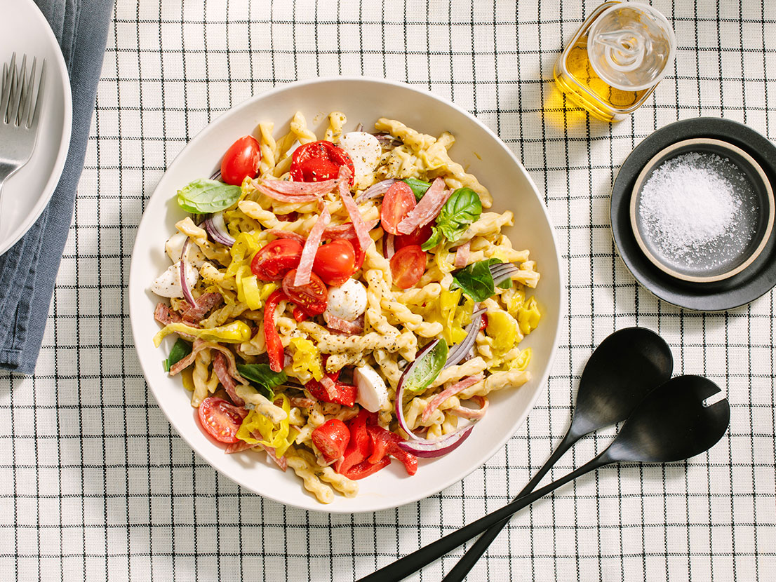An image of prepared Creamy Pesto Antipasto Salad made with gemelli, Prego® Creamy Basil Pesto Sauce, cherry tomatoes, mozzarella, pepperoncini, red pepper, artichoke heads and salami or pepperoni.
