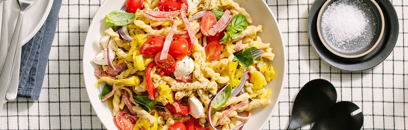 An image of prepared Creamy Pesto Antipasto Salad made with gemelli, Prego® Creamy Basil Pesto Sauce, cherry tomatoes, mozzarella, pepperoncini, red pepper, artichoke heads and salami or pepperoni.