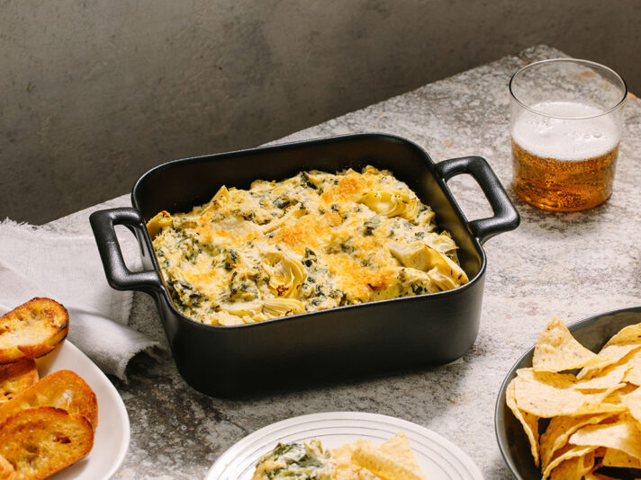 An image of prepared Pesto Spinach and Artichoke Dip made with artichoke hearts, garlic, Prego® Creamy Parmesan Pesto Sauce, cream cheese and spinach.